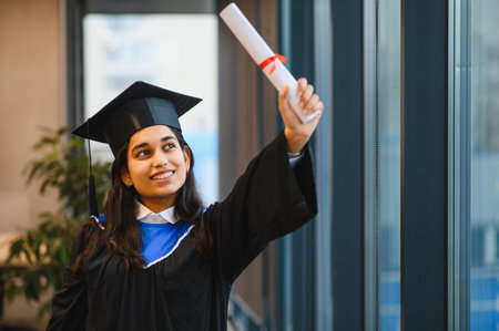 Indian student celebrating graduation day, holding a rolled diploma. Achieving academic success and showing happiness at universityの写真素材