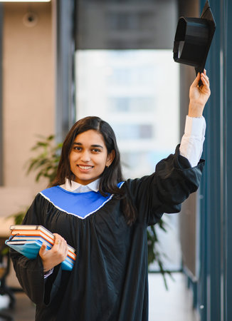 Indian female student wearing a graduation gown and holding books, celebrating her academic achievement and future successの写真素材