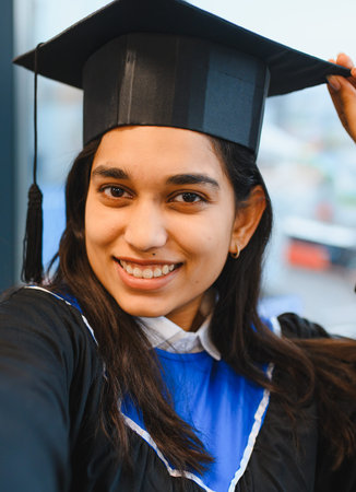 Indian female student wearing a graduation cap and gown, smiling at her academic achievement and completing her studiesの写真素材