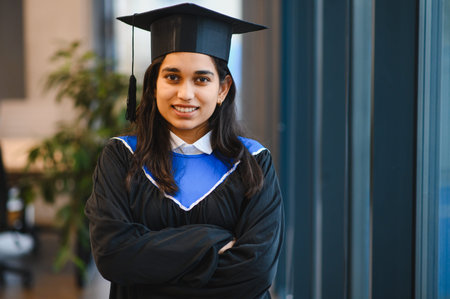 Young Indian woman wearing academic gown and mortarboard, smiling and celebrating graduation achievementの写真素材
