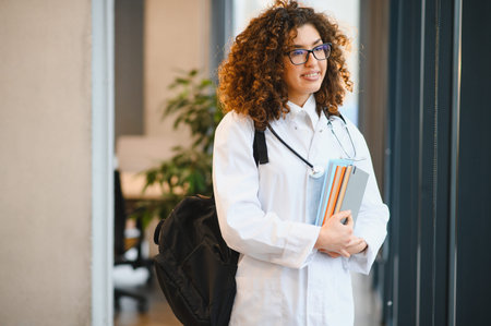 Young female medical student carrying textbooks and backpack, smiling and looking forward in a university hallの写真素材