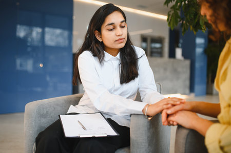Indian female psychologist showing empathy and support to patient during counseling, holding her hand. Mental health assistance and understandingの写真素材