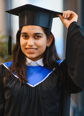 Female south asian student proudly wearing a graduation cap and gown, smiling at the camera, celebrating academic achievementの写真素材