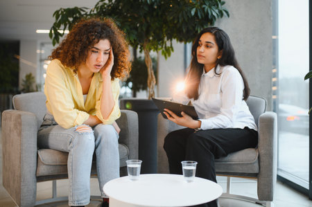 Indian psychologist counseling a female patient experiencing anxiety during a therapy session in a modern office setupの写真素材