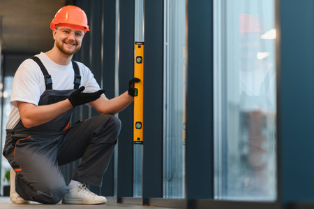 Construction worker wearing hard hat and safety glasses, using a bubble level for accurate...
