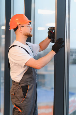 Young professional construction worker wearing hard hat and safety glasses using a power drill to install a window frameの写真素材