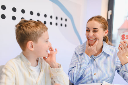 Speech therapist working with a child on pronunciation, showing a letter card and guiding jaw movement. Learning communication skillsの写真素材