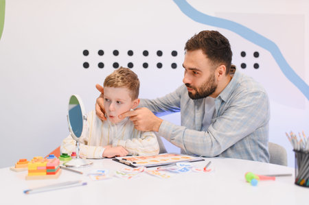 Speech therapist assisting a young boy with articulation exercises in front of a mirror, focusing on speech developmentの写真素材