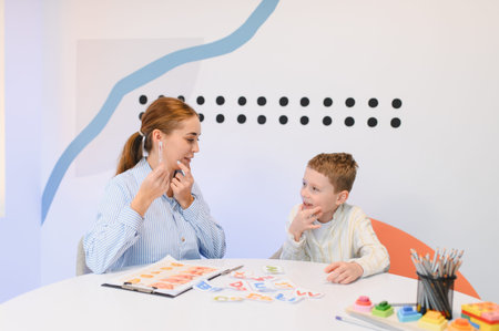 Speech therapist with a boy during a session, helping with articulation using a tool and letter...