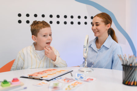 Young boy articulating sounds, practicing speech development with a female logopedist during a session, using a mirror and cardsの写真素材