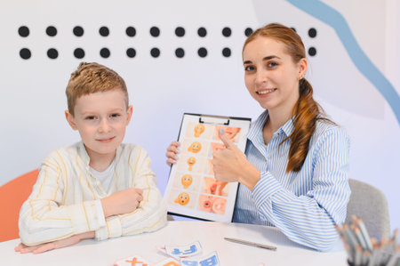 Young female therapist teaching boy how to recognize and express emotions using an emoji chart during a sessionの写真素材