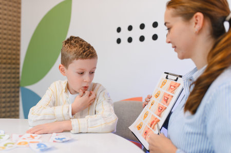 Young boy training articulation and communication skills with a specialist, looking at a board with mouth exercisesの写真素材