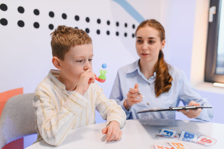 Child learning speech skills during developmental lesson, blowing ball with therapist in a bright, modern clinic environmentの写真素材