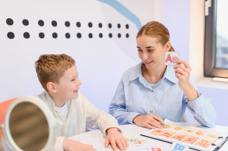 Speech therapist showing an alphabet card to a boy, helping with language development and...