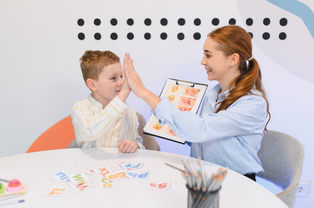 Young boy client high fiving a speech language pathologist during a therapy session, celebrating...