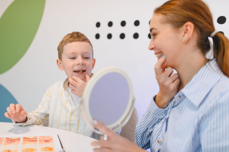 Speech therapist assisting a young boy with articulation and pronunciation exercises, using a mirror...