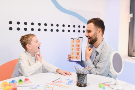 Male speech therapist guiding a young boy through mouth exercises using visual aids for improved articulation and communication skillsの写真素材