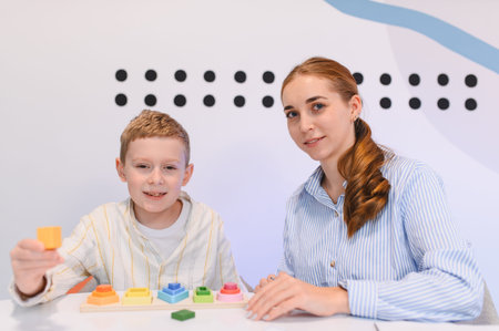 Boy playing with colorful educational wooden blocks, sort practicing and stacking. Teacher assisting...