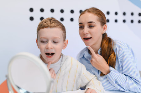 Speech therapist guiding a boy in articulation exercises using a mirror for speech development and...