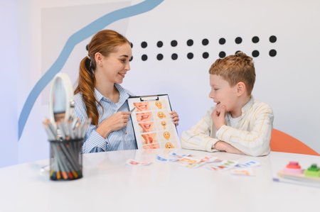 Female speech therapist helping a young boy with speech therapy exercises in a modern classroom settingの写真素材