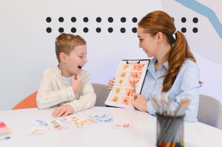 Woman speech therapist working with a young boy, using a chart with mouth expressions and emojis during a communication sessionの写真素材