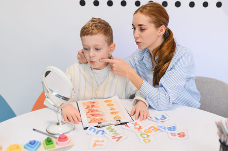 Speech therapist helping child with speech development. Little boy learning proper mouth movements looking in a mirror during therapy sessionの写真素材