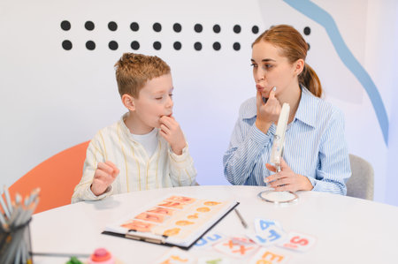 Speech therapist helping a boy with articulation exercises during therapy. They are using mouth shape cards and a mirror for practiceの写真素材