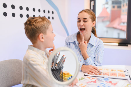 Speech therapist working with a young boy, demonstrating proper mouth and tongue positioning during...