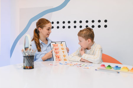 Therapist showing mouth exercises and emotional cards to a young boy during a developmental therapy sessionの写真素材