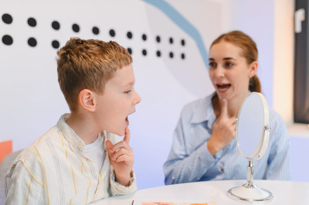 Young boy learning articulation exercises with a speech therapist. They are using a mirror for visual feedback during the sessionの写真素材