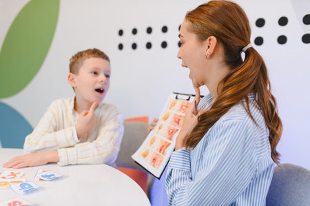 Speech pathologist working with a young boy to improve pronunciation and communication skills using visual aids in a therapy sessionの写真素材