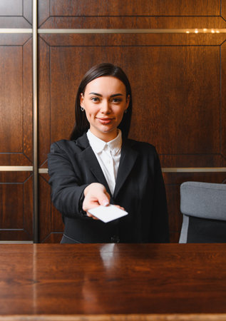 Professional woman at hotel reception desk providing a blank room key card, offering hospitality serviceの写真素材