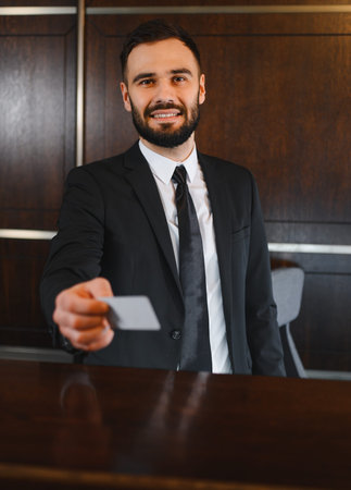 Smiling hotel receptionist in suit hands key card to guest at modern front desk, welcoming and...
