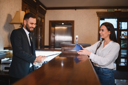 Smiling woman handing passport to a friendly hotel receptionist, completing check in procedures at wooden reception deskの写真素材