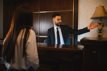 Hotel receptionist man interacting with a woman guest, offering assistance and hospitality service in the lobbyの写真素材