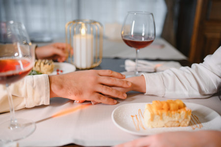 Couple holding hands across a table during a romantic dinner, sharing wine and dessert by candlelight in a restaurantの写真素材