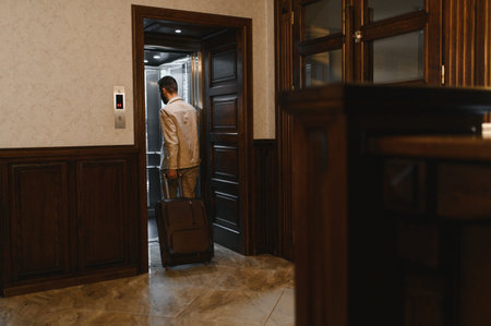 Man with a suitcase entering an open elevator in a classic hotel lobby, representing travel, business trips, and arrivalの写真素材