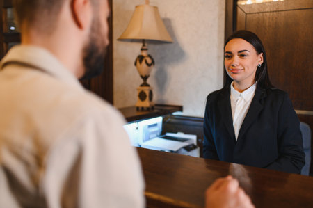 Hotel receptionist smiling, assisting a guest arriving at the reception desk in a hotel lobby, providing serviceの写真素材
