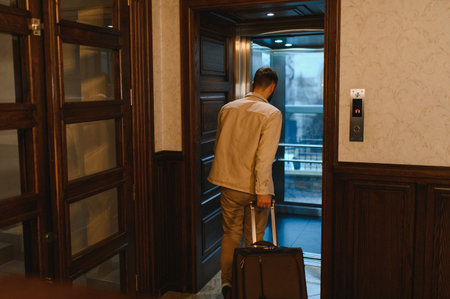 Man with travel luggage entering a modern hotel elevator, preparing for his trip or leaving after his stayの写真素材