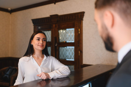 Female receptionist smiling and working, providing excellent service to a guest at the front desk in a hotel lobbyの写真素材