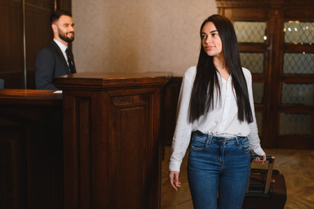 Woman pulling luggage in hotel lobby, receptionist standing at desk, creating a scene of arrival and hospitality serviceの写真素材