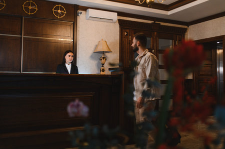 Professional female receptionist welcoming a male guest at a hotel lobby reception desk providing service and accommodationの写真素材