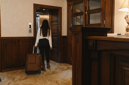 Woman pulling luggage in a hotel lobby, going to an elevator for check in or departure, representing modern hospitality and travelの写真素材