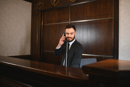Hotel receptionist providing excellent guest service, answering a telephone call from behind a...