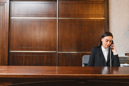 Receptionist working at a hotel front desk, speaking on landline phone, providing customer service in the lobbyの写真素材