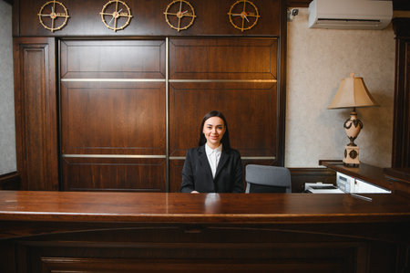 Professional woman working at a hotel front desk, offering a welcoming smile and quality hospitality service in a modern lobbyの写真素材