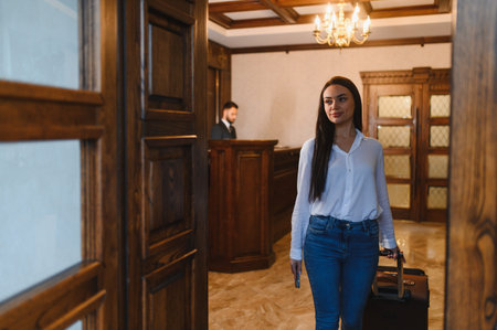 Woman arriving at a hotel, pulling a suitcase through the elegant lobby. Receptionist working at the front desk in backgroundの写真素材