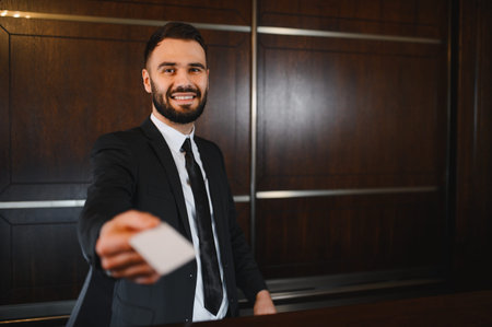 Friendly hotel receptionist standing at the lobby desk, extending a blank plastic key card to a guest for check inの写真素材