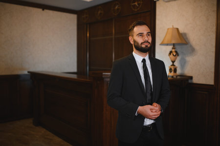 Professional man in a black suit standing in a hotel lobby, portraying concepts of service, hospitality, and welcomingの写真素材