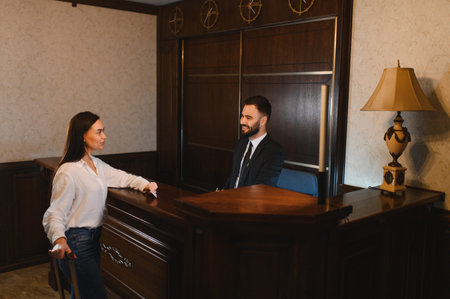 Guest standing at a luxurious hotel reception desk, interacting with a smiling male receptionist...